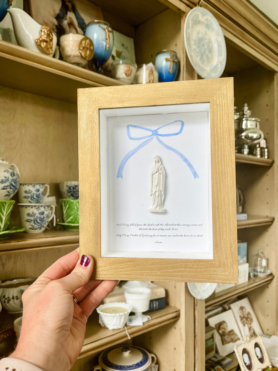 Hail Mary in display case  with blue bow- Mary Abraham Collective